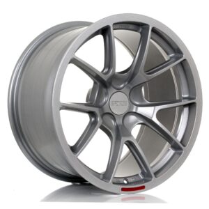 Silver alloy car wheel with multiple spokes and a central Forged cap, facing at an angle with a red alignment marker near the rim
