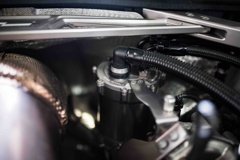 Close-up of a car’s engine bay showing braided hoses, metal fittings, and dark plastic connectors.