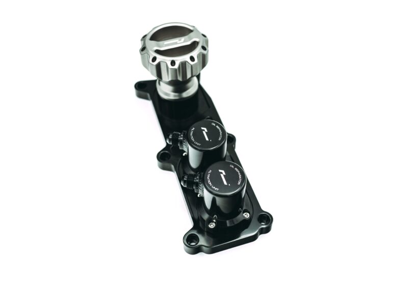 Close-up of a metallic handlebar clamp/dial on a black bicycle/motorcycle component with adjustment knobs.