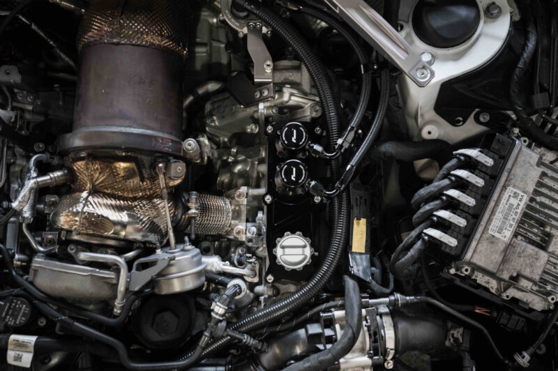 Close-up of a car engine bay showing a turbocharger, hoses, and wiring.