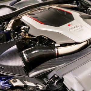 49655209046_24d564d6d3_k-1jpg - OPSHOLDERS Close-up under the hood of an Audi sports car, showing a silver engine cover with the Audi rings and red accents amid carbon-fiber panels.