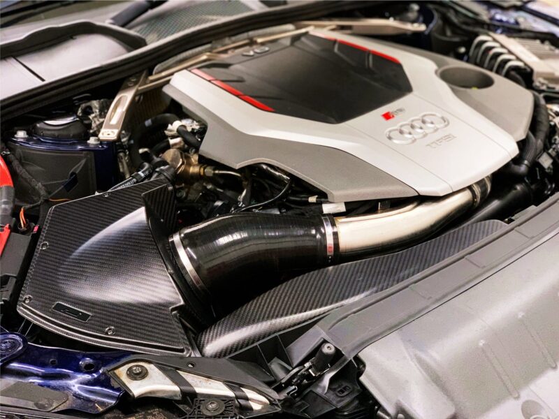 49655209046_24d564d6d3_k-1jpg - OPSHOLDERS Close-up under the hood of an Audi sports car, showing a silver engine cover with the Audi rings and red accents amid carbon-fiber panels.