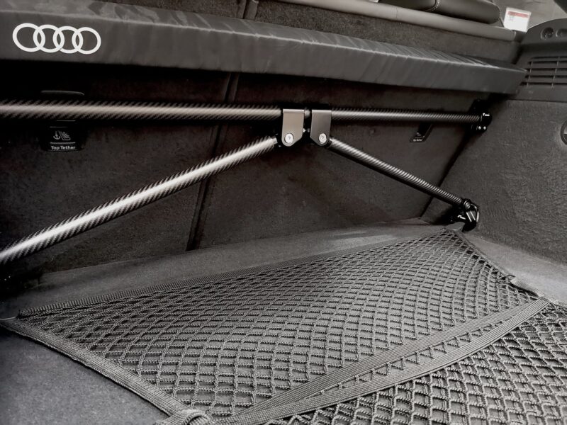 50813847421_e2fe8ff419_k-2jpg - OPSHOLDERS Interior of a car trunk with carbon-fiber support rails, a mesh cargo net, and an Audi logo trim edge.