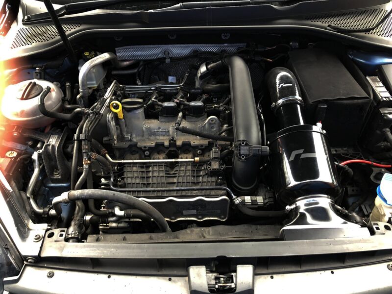 Front view of a car engine bay with hoses, battery, and intake tube visible under the hood across the frame