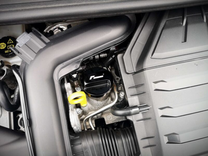 Open vehicle compartment showing engine bay area with hoses, wiring, and a yellow dipstick handle visible near the edge of the opening (likely a maintenance space).