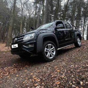 53272648840_054c5488e1_k-1jpg - OPSHOLDERS Black pickup truck parked on a leaf-covered forest path with trees in the background, seen from the front-left angle.