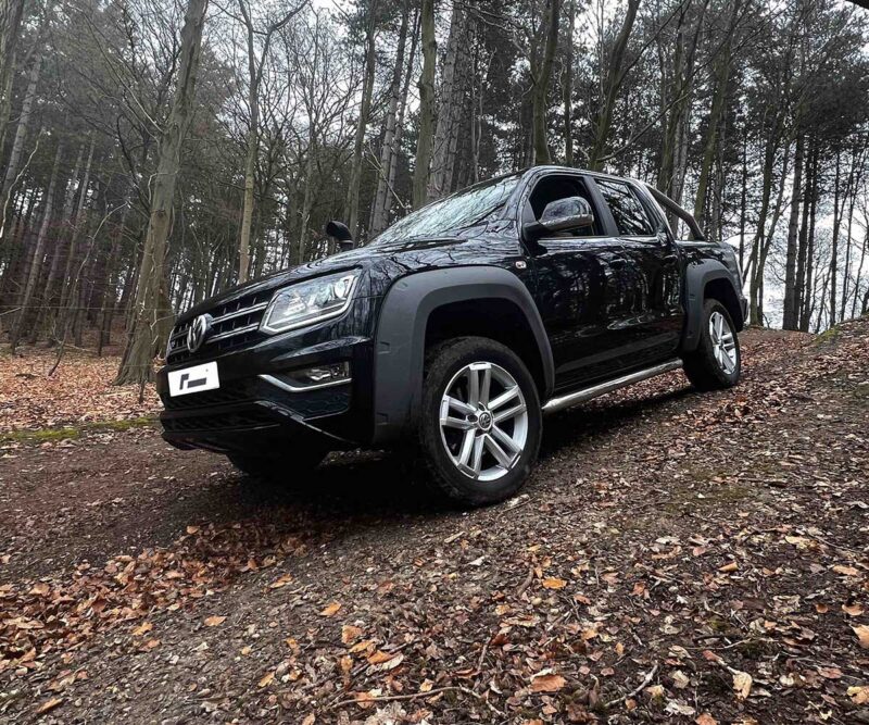 53272648840_054c5488e1_k-1jpg - OPSHOLDERS Black pickup truck parked on a leaf-covered forest path with trees in the background, seen from the front-left angle.