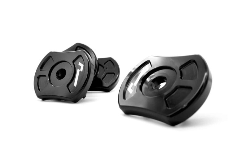 Close-up of black metal locking collars with a central hole and white markings, scattered on a white background; likely bicycle or mechanical components used to secure parts.