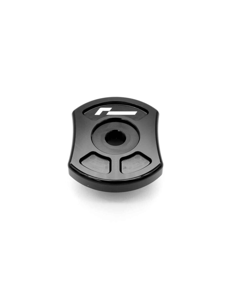 Close-up of a black plastic component with a circular central recess and two gray grip pads at the bottom, partially showing a logo on the top surface.