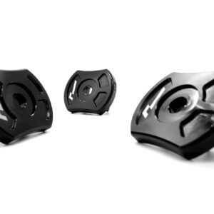 Three black circular metal components with cutouts arranged on a white background, seen from a low angle on a clean surface.