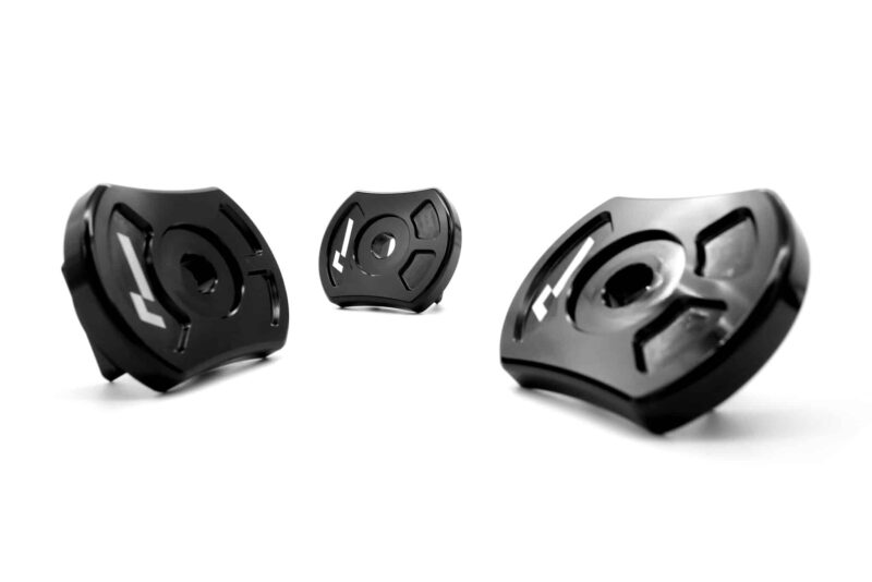 Three black circular metal components with cutouts arranged on a white background, seen from a low angle on a clean surface.