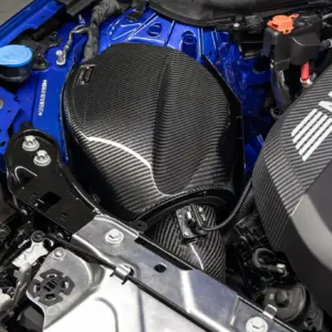 Close-up of a blue BMW engine bay featuring a carbon fiber intake cover and visible battery area.