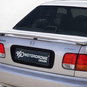 Rear view of a silver Honda Civic with a spoiler and a black Motordrome Design plate on the trunk.