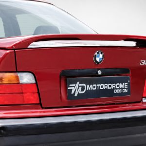 Rear view of a red BMW 325i showing the trunk, badge, and a Motordrome Design plate in the center.