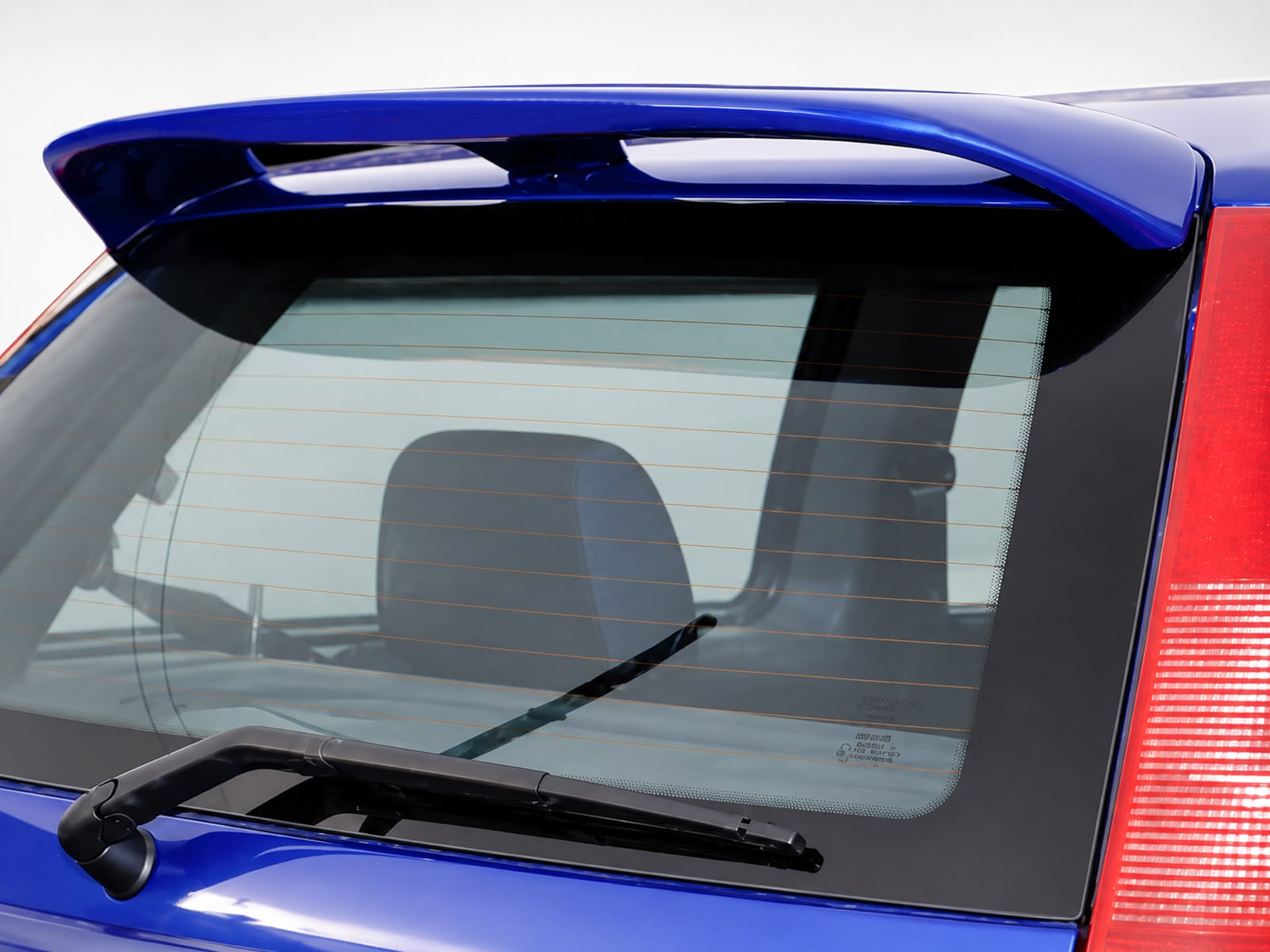 A-143_1jpg - OPSHOLDERS Blue hatchback rear window with defroster lines and a wiper, showing part of the tail light and spoiler edge
