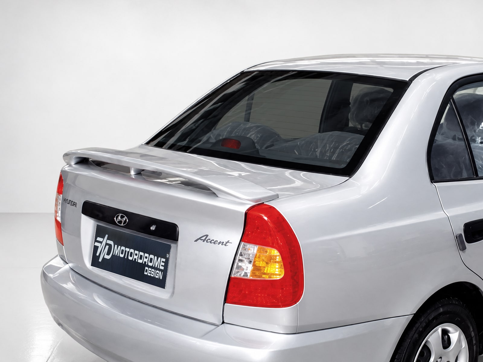 A-169_1jpg - OPSHOLDERS Rear of a silver Hyundai Accent with a large rear spoiler and red tail lights in a studio setting
