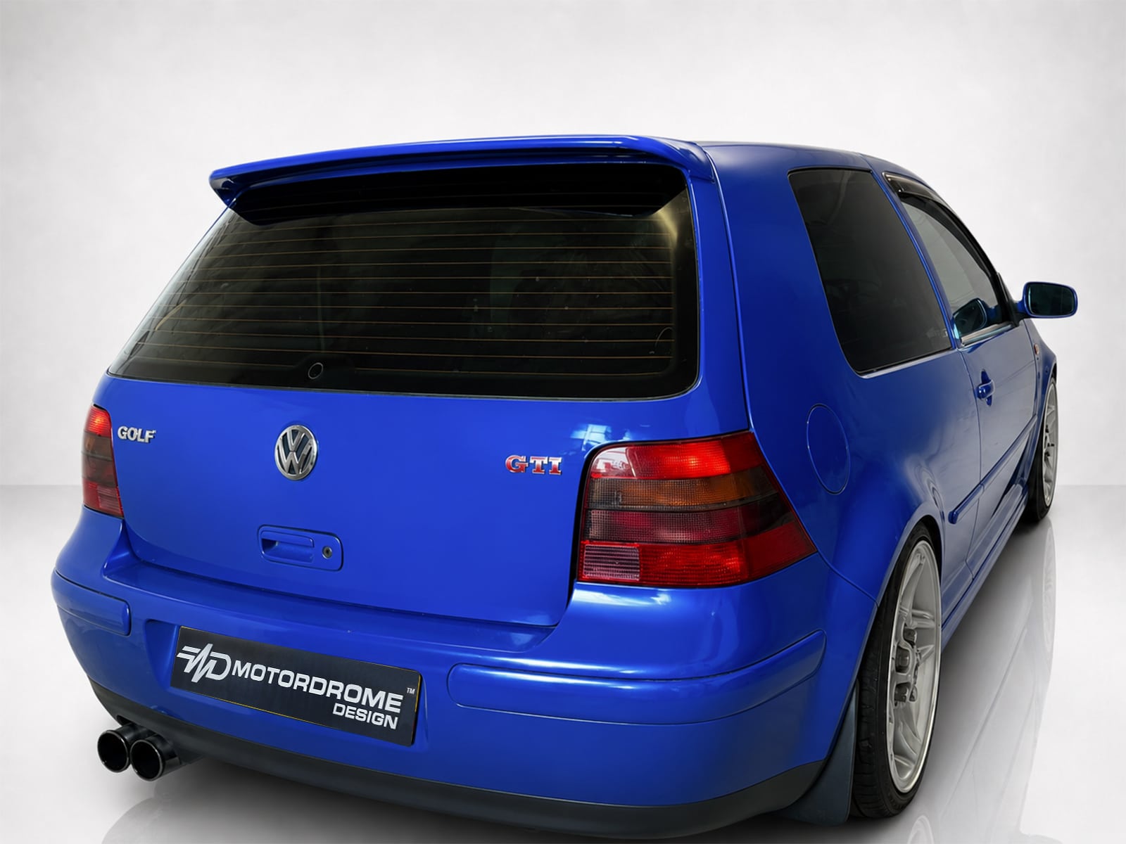 A-201_1jpg - OPSHOLDERS Blue Volkswagen Golf GTI hatchback shown from the rear-right side with a spoiler and dual exhausts visible