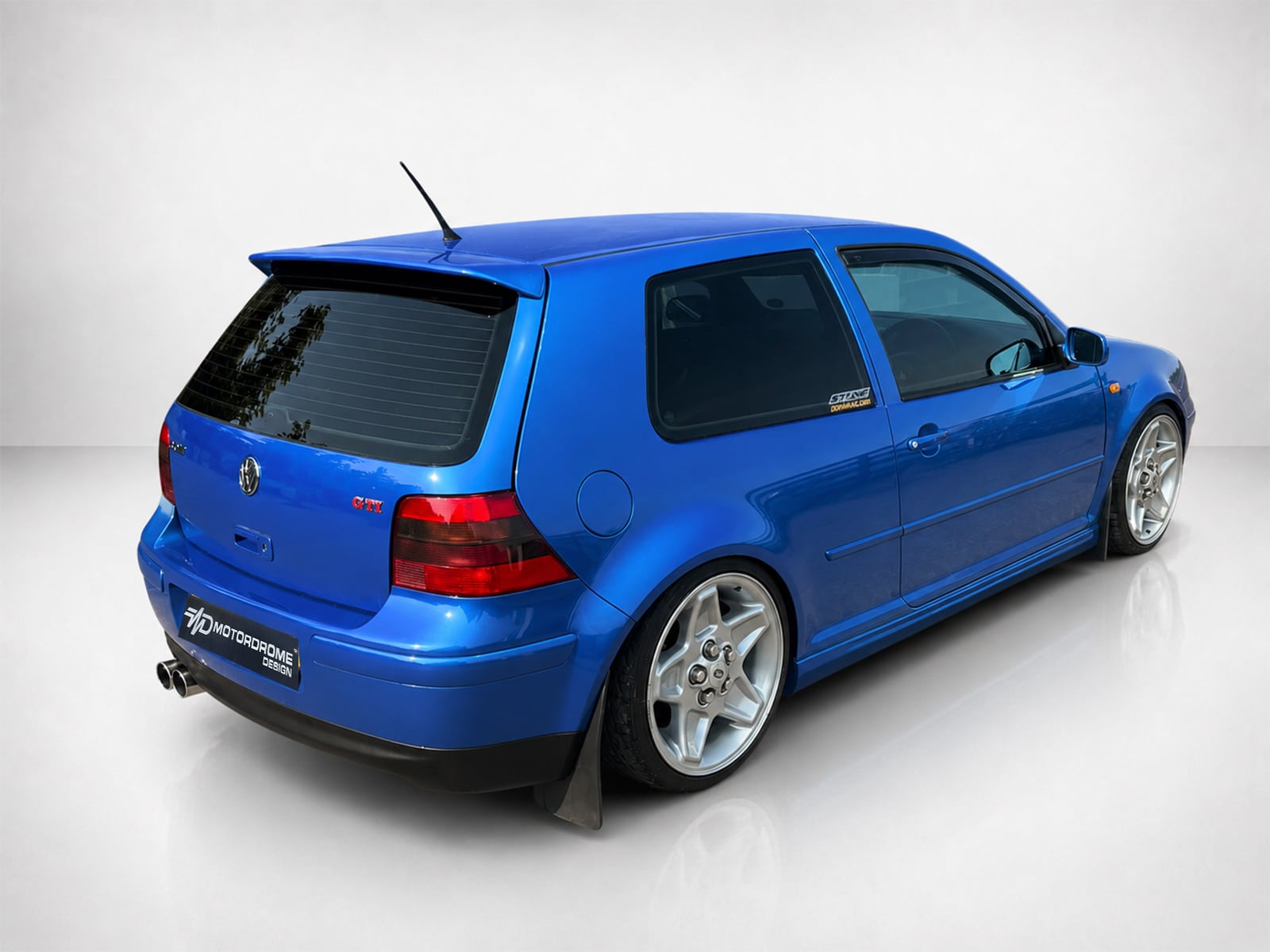 A-201_2jpg - OPSHOLDERS Blue modified hatchback viewed from the rear-left, featuring aftermarket wheels and a rear spoiler/roof antenna.