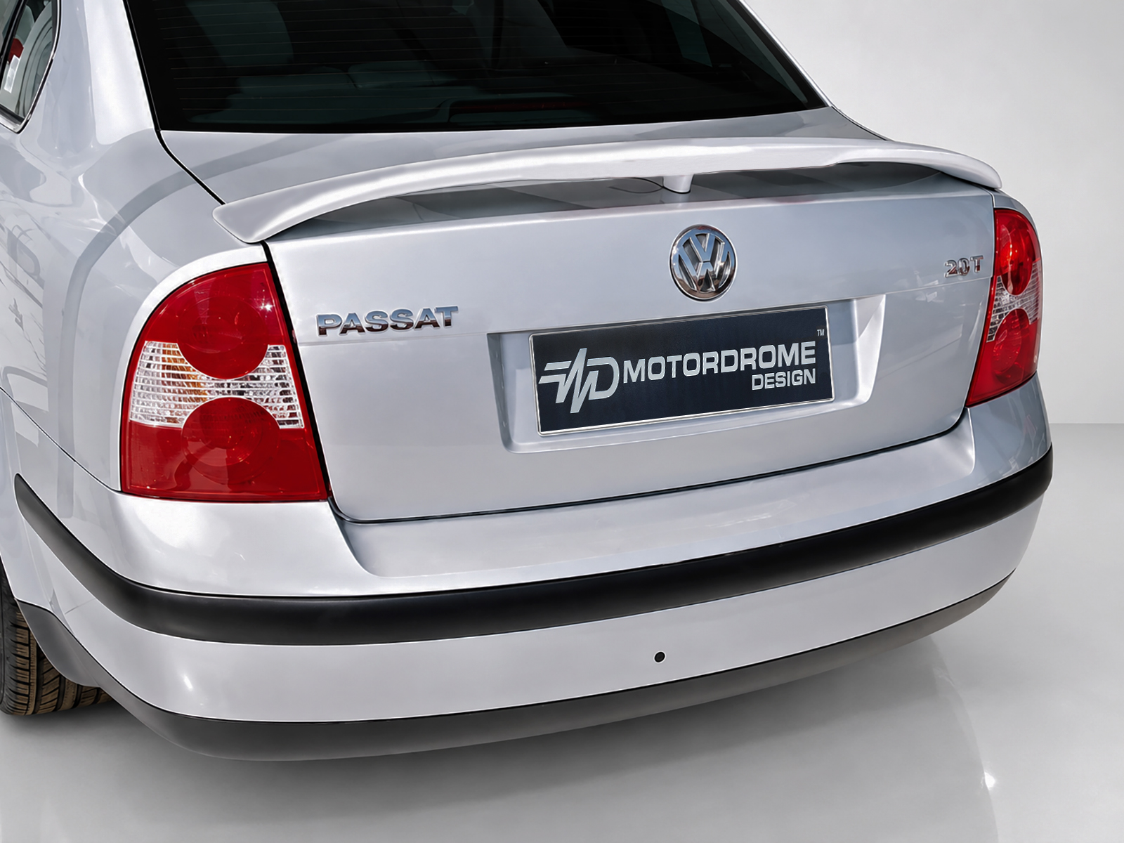 A-204_1jpg - OPSHOLDERS Rear view of a silver Volkswagen Passat, showing taillights, badges (PASSAT, 2.0T) and a dark Motordrome Design plate on the trunk team area