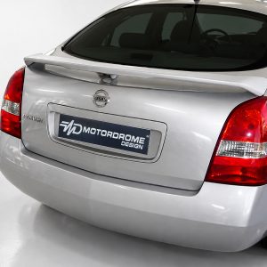 Rear view of a silver Nissan Primera hatchback with a Motordrome Design branded license plate and visible taillights under showroom lighting