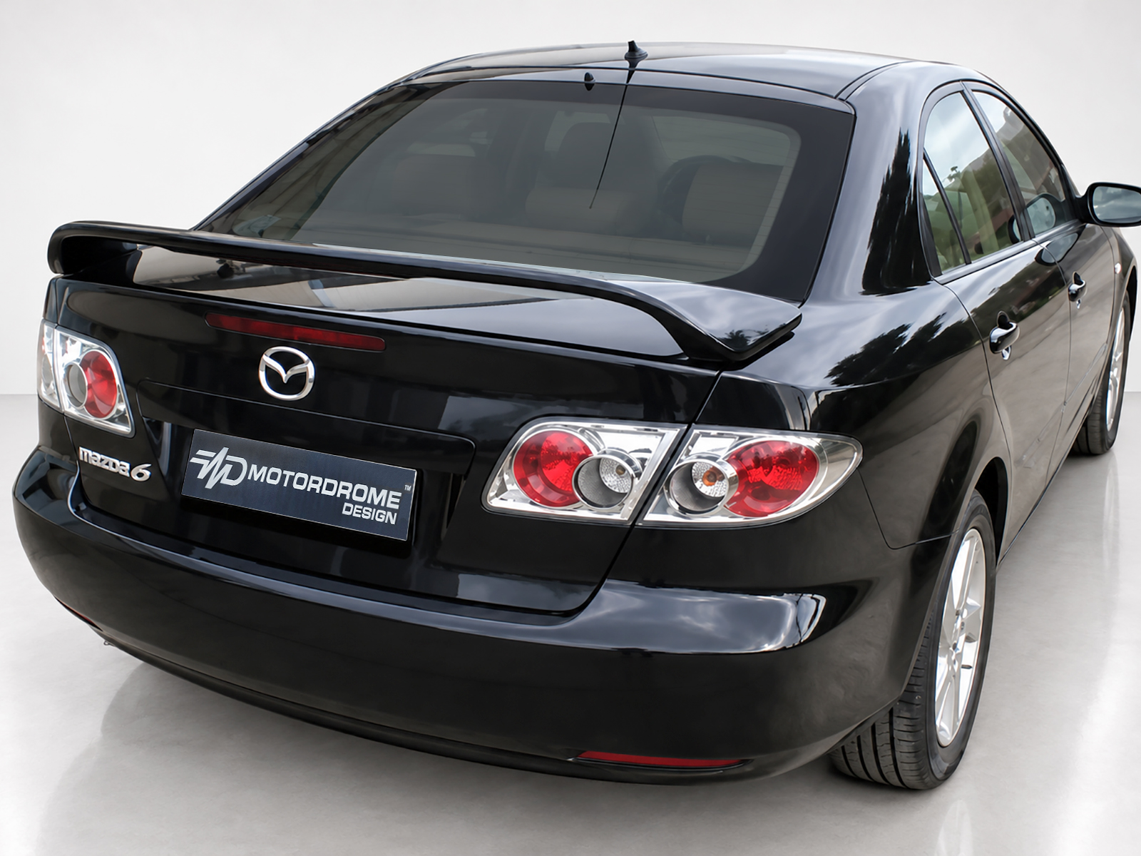 A-263_1jpg - OPSHOLDERS Rear three-quarter view of a glossy black Mazda 6 with a rear spoiler and a Motordrome Design plate on the tailgate.