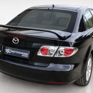 Black Mazda6 rear view with spoiler in a showroom; license plate reads MOTORDROME DESIGN