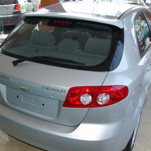 Silver Chevrolet hatchback viewed from the rear inside a showroom, showing taillights and rear window.