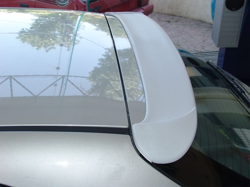 Close-up of a silver car's rear spoiler mounted above the rear window, showing its curved aerodynamic shape.