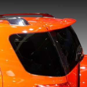 Orange SUV seen from the rear side, with tinted windows and a roof rack against a gray gradient background.