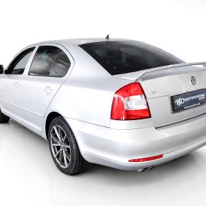 Rear three-quarter view of a silver sedan in a white studio, showing taillights and rear spoiler (Skoda model).