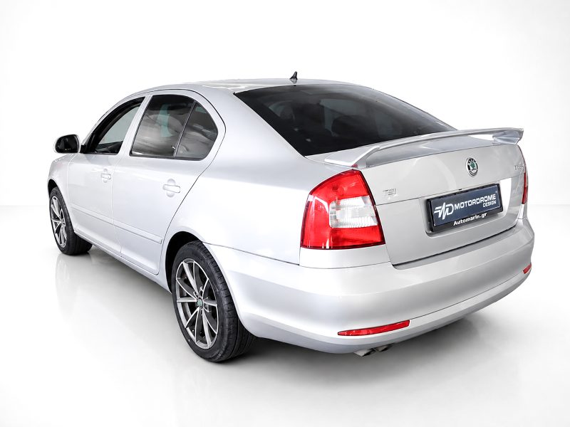 Rear three-quarter view of a silver sedan in a white studio, showing taillights and rear spoiler (Skoda model).