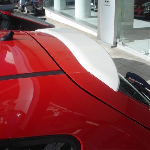 Close-up of a bright red car roof with a white aerodynamic fin/antenna near the rear window at a dealership showroom.