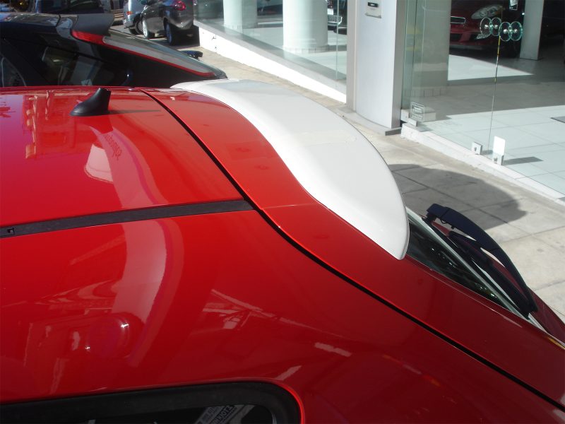Close-up of a bright red car roof with a white aerodynamic fin/antenna near the rear window at a dealership showroom.