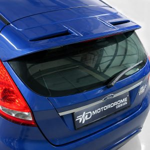 Blue Ford hatchback rear with spoiler, rear vents, wiper, and red taillight; Motordrome Design plate visible on the tailgate.