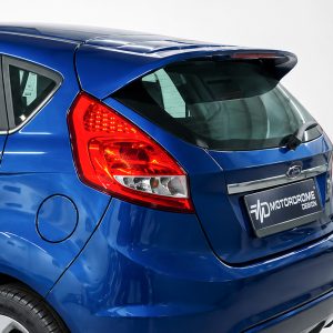 Blue hatchback rear with large red taillight and a branded license plate reading MOTORdROME DESIGN on a light backdrop.