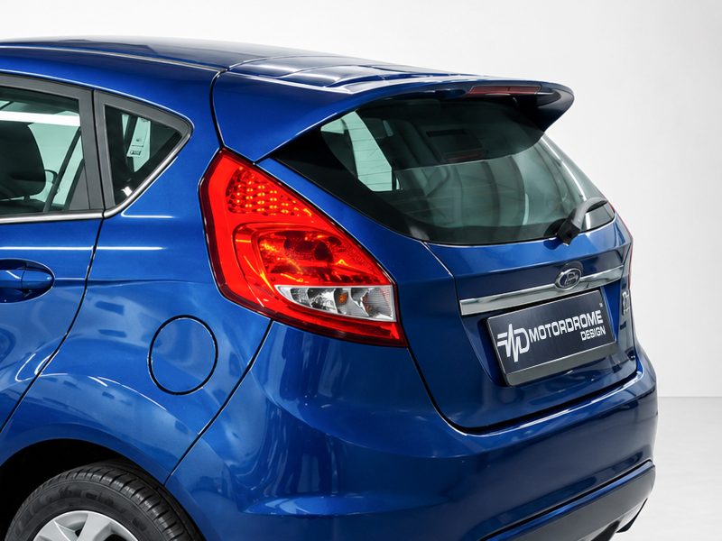 Blue hatchback rear with large red taillight and a branded license plate reading MOTORdROME DESIGN on a light backdrop.