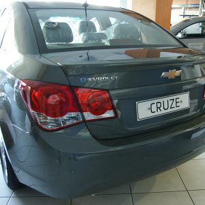 Rear view of a gray Chevrolet Cruze in a dealership showroom, showing tail lights, Chevy badge, and license plate CRUZE.