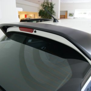 Close-up of a white car's rear window, roof spoiler, antenna, and taillight in a showroom setting