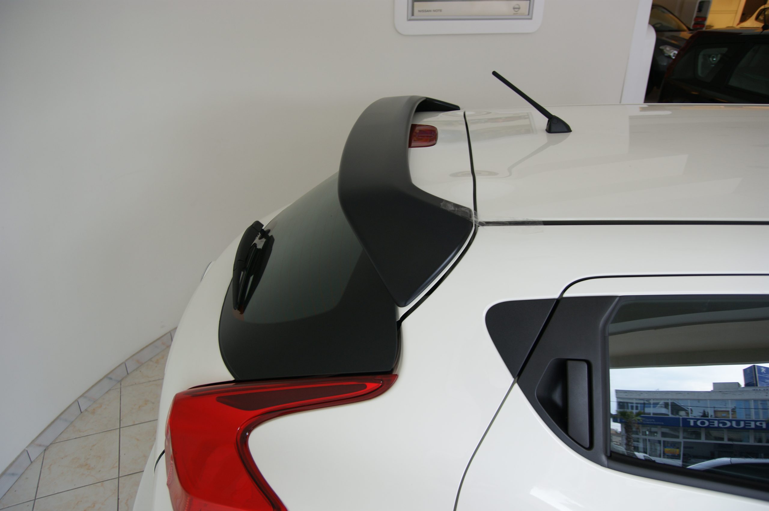 SONY DSC - OPSHOLDERS Rear view of a white SUV showing a black rooftop spoiler, antenna, and red taillights in a showroom setting.