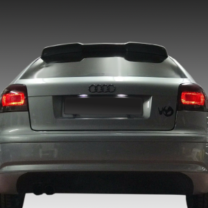 Rear view of a silver Audi with a rear spoiler, illuminated taillights, and a blurred license plate area against a gradient background.