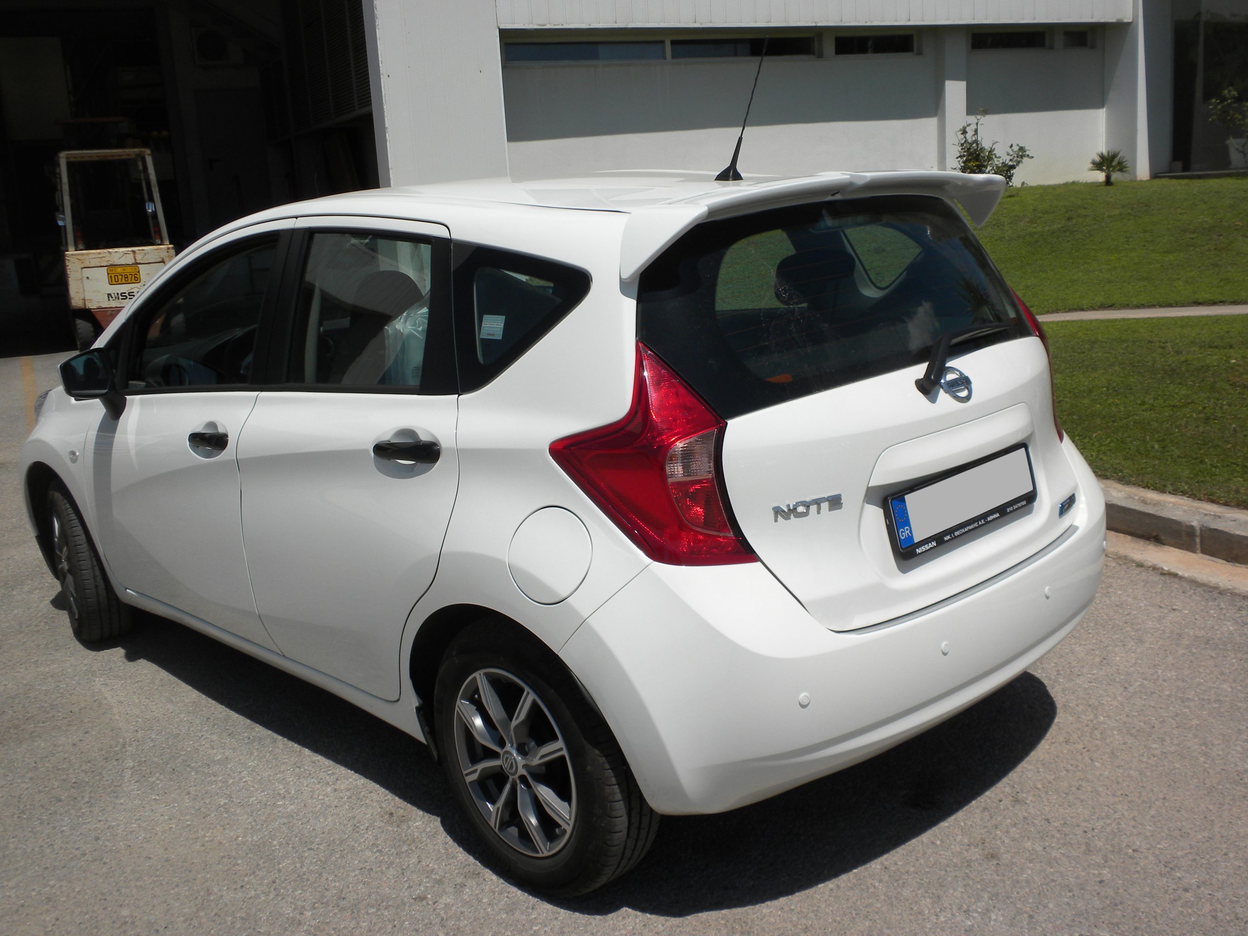 A-401_1jpg - OPSHOLDERS White Nissan Note hatchback parked in a sunny parking lot, rear three-quarter view with taillights visible