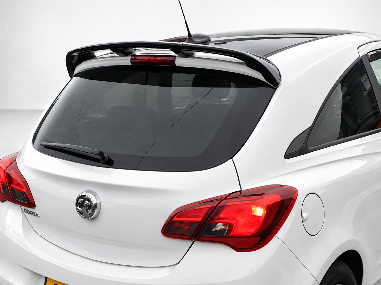 A-407_1jpg - OPSHOLDERS White hatchback car rear with integrated spoiler and rear window wiper, showing red taillights and Opel/Vauxhall Corsa badge