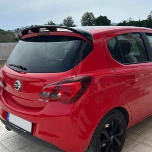 Red hatchback car parked on a light tiled driveway, rear view showing the Opel badge and a small rear spoiler on the roof edge.