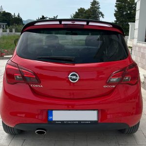 A-408_2jpg - OPSHOLDERS Rear view of a red Opel Corsa EcoFlex parked on a tiled driveway beside a house. The trunk, rear lights, and exhaust are visible with a Greek license plate.
