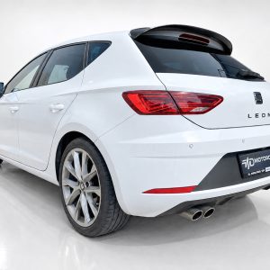 Rear three-quarter view of a white SEAT Leon hatchback in a bright studio setting, showing distinctive taillights and dual exhausts.