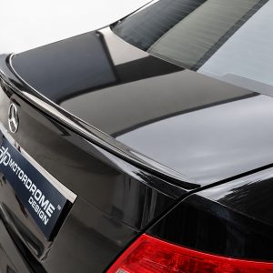 Rear view of a glossy black Mercedes-Benz showing the trunk, chrome trim, emblem, and red taillight; dealer plate visible on the back.