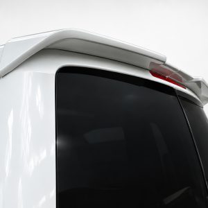 Rear corner of a white van showing a curved roof spoiler and dark tinted rear window