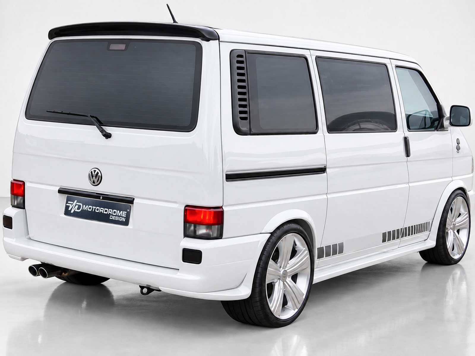 A-421_2jpg - OPSHOLDERS White VW minivan shown from rear and side, featuring large chrome aftermarket wheels and gray decal accents along the lower body plate reading Motordrome Design