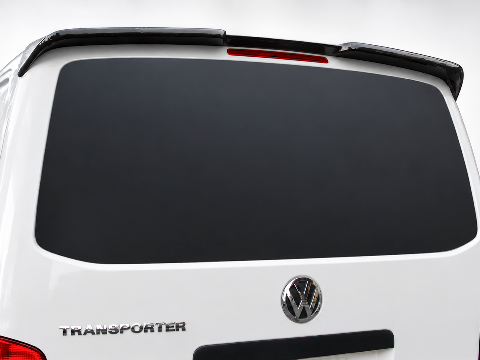 A-423_2jpg - OPSHOLDERS Rear view of a white Volkswagen Transporter van with a large dark rear window and VW badge visible on the tailgate, slight spoiler across the top edge.