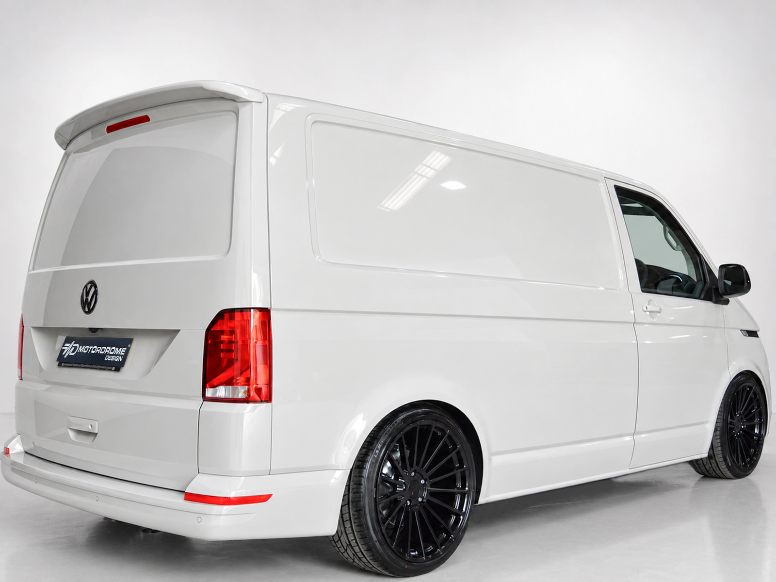 A-425_1jpg - OPSHOLDERS Rear-right view of a white cargo van with a large side panel, VW emblem, red taillights, and black aftermarket wheels.